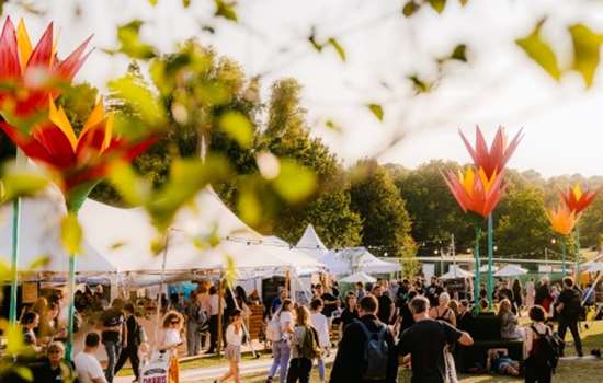 An outdoor festival with crowds of people walking among large white tents and sculptures of flowers. 