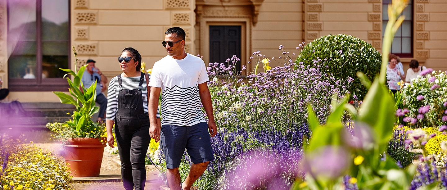 Two people holding hands walk through Osborne House gardens in the sunshine.