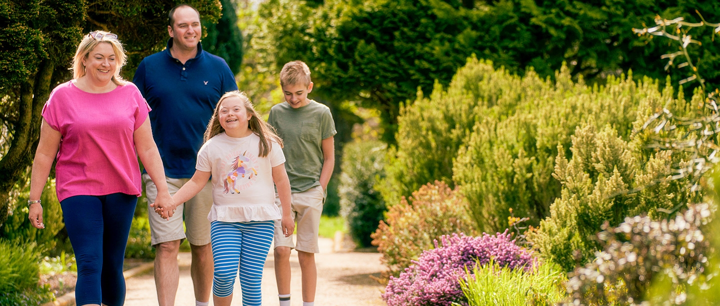 Photo of two adults and two children smiling and walking through a historic garden on a sunny day