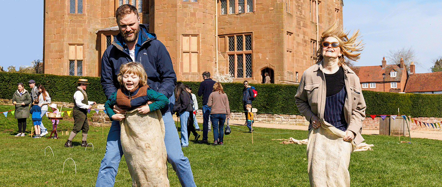 Photo of two adults and a child doing a sack race in front of Kenilworth Castle in Warwickshire